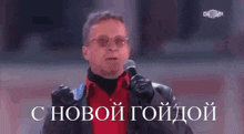 a man in a red shirt is holding a microphone in front of a sign that says " с новой годдой "