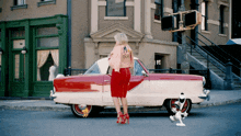 a woman in a red skirt stands next to a red and white car