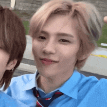 a young man wearing a blue shirt and tie is taking a selfie .