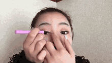 a woman is applying eye shadow to her eye with a pink marker .