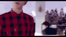 a man in a red and black plaid shirt and tie is standing in front of a mirror .