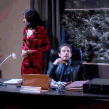 a man sits at a desk with a sign that says jake dimera on it