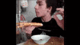 a man eating a slice of pizza next to a bowl with ketchup