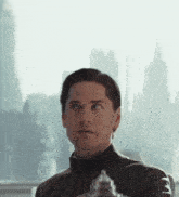a man in a black turtleneck looks out a window with a city in the background
