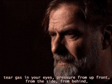 a man with a beard has tear gas in his eyes and pressure from up front from the side and from behind