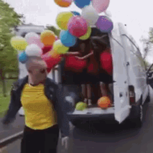 a man is holding balloons in front of a van .