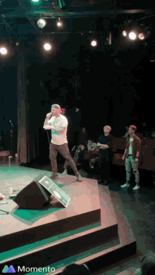 a man stands on a stage holding a microphone and the word momento is on the bottom