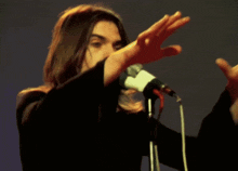a man with long hair singing into a microphone with his hands