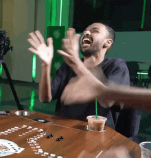 a man is sitting at a table with his hands in the air and a starbucks drink in his hand .