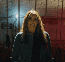 a woman in a denim jacket is smiling in front of a red wall