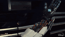 a woman in a red jacket holds a robotic hand in front of a sign for ironheart