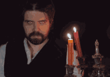 a man with red eyes and a beard stands in front of a bunch of lit candles