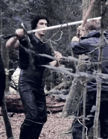a man in a black shirt is holding a sword while standing in the woods .