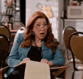 a woman wearing glasses is sitting in a chair holding a notebook and a pen .