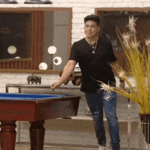 a man in a black shirt is standing next to a pool table in a room