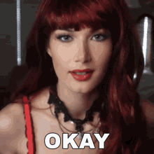 a woman with red hair is wearing a necklace and says okay