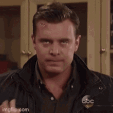 a man with a scar on his forehead is wearing a black jacket .