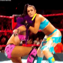 two women are wrestling in a ring and one of them is wearing a pink top .