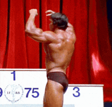 a man flexes his muscles in front of a podium with the number 75 on it