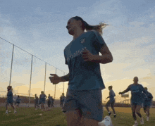 a woman wearing a blue shirt that says herbalife is running on a field
