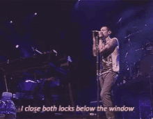 a man singing into a microphone with the words i close both locks below the window above him
