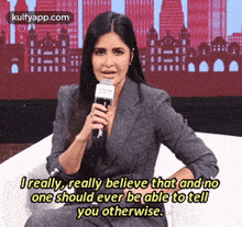 a woman in a suit is sitting on a couch holding a microphone and talking into it .