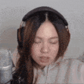 a woman wearing headphones and a hoodie is sitting in front of a microphone .