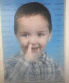 a little boy holds his finger to his nose