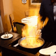 a man in a suit is cooking with flames coming out of a frying pan