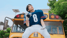 a boy wearing a jersey with the number 8 on it is standing on a school bus