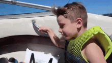 a young boy wearing a life jacket is sitting on a boat holding a bag with the letter v on it