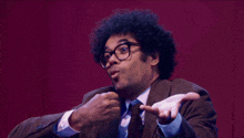 a man with curly hair and glasses says softly what are you gonna do in front of a red wall