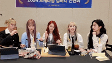 a group of girls are sitting around a table with a sign that says 2024 on it