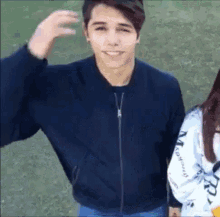 a young man in a blue jacket is standing next to a girl in a white sweatshirt .