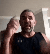 a man with a beard wearing a black tank top is making a funny face .