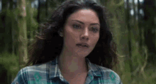 a woman in a plaid shirt stands in the woods