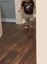a baby wearing a black shirt that says rock n roll is running on a wooden floor
