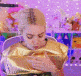a woman is wearing a gold shirt and holding a gold bag in her hands .