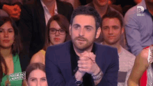 a man in a suit is sitting in front of a crowd with a sign that says touche pas a mon poste .