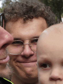 a close up of a man wearing glasses and holding a baby
