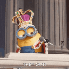 a minion wearing a crown and a king 's robe is speaking into a microphone and says they out