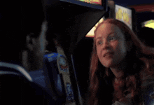 a woman with red hair is sitting in front of an arcade machine