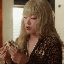 a woman in a leopard print jacket is holding a sandwich in her hands
