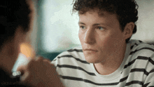 a man with curly hair wearing a striped shirt is looking at another man .