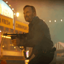 a man holding a gun in front of a sign that says fresh cinnamon
