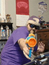 a man in a purple shirt is holding a water gun in front of a sign that says electrify umbrella
