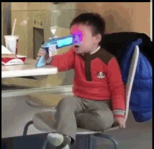 a young boy in a red shirt is sitting in a chair holding a toy gun