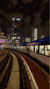 a train is going down the tracks at night with buildings in the background