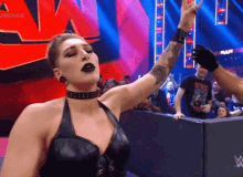a woman in a black leather dress is standing in front of a crowd and raising her hand in the air .