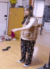 a woman in a vest and floral pants is standing on a wood floor